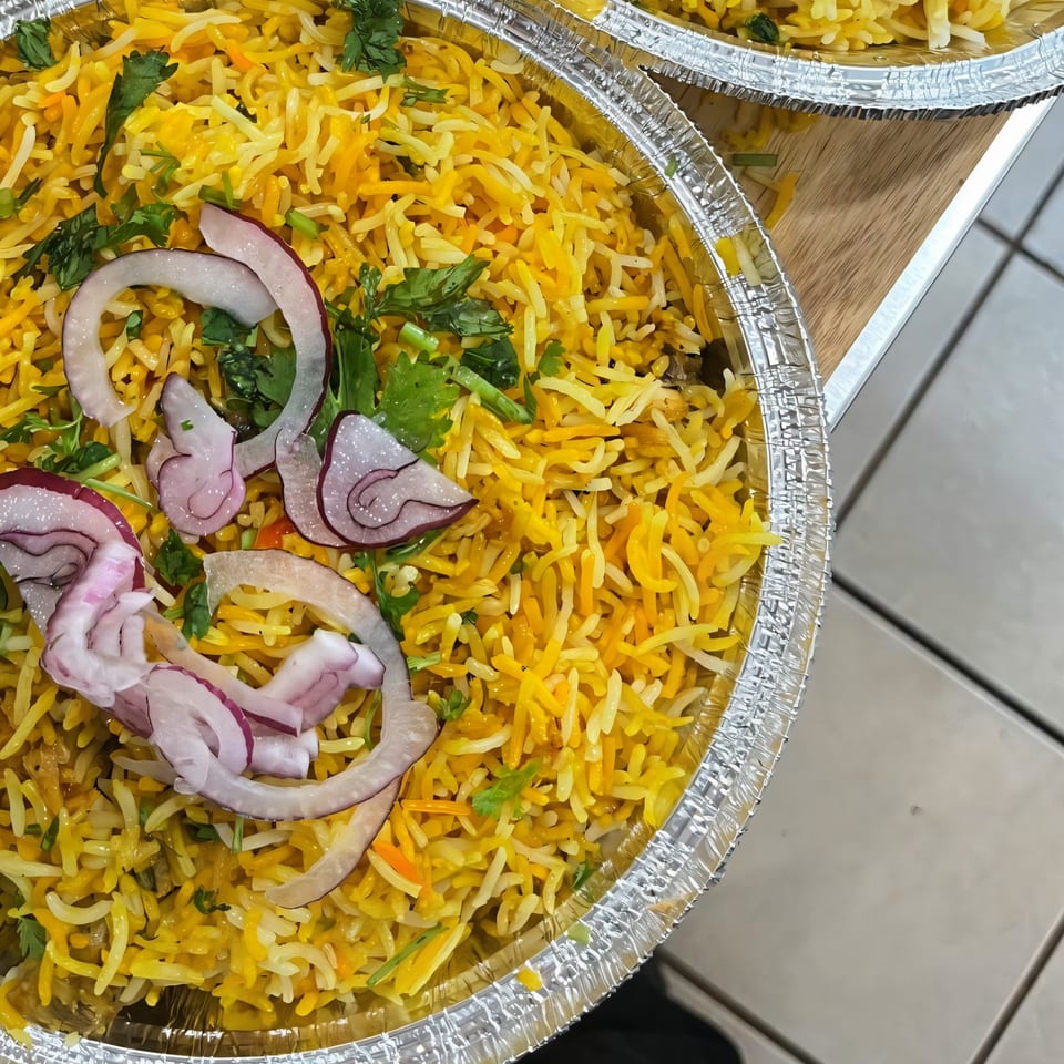 Ellenville Spice Fusion's chicken biryani with red onions and cilantro in a foil container.