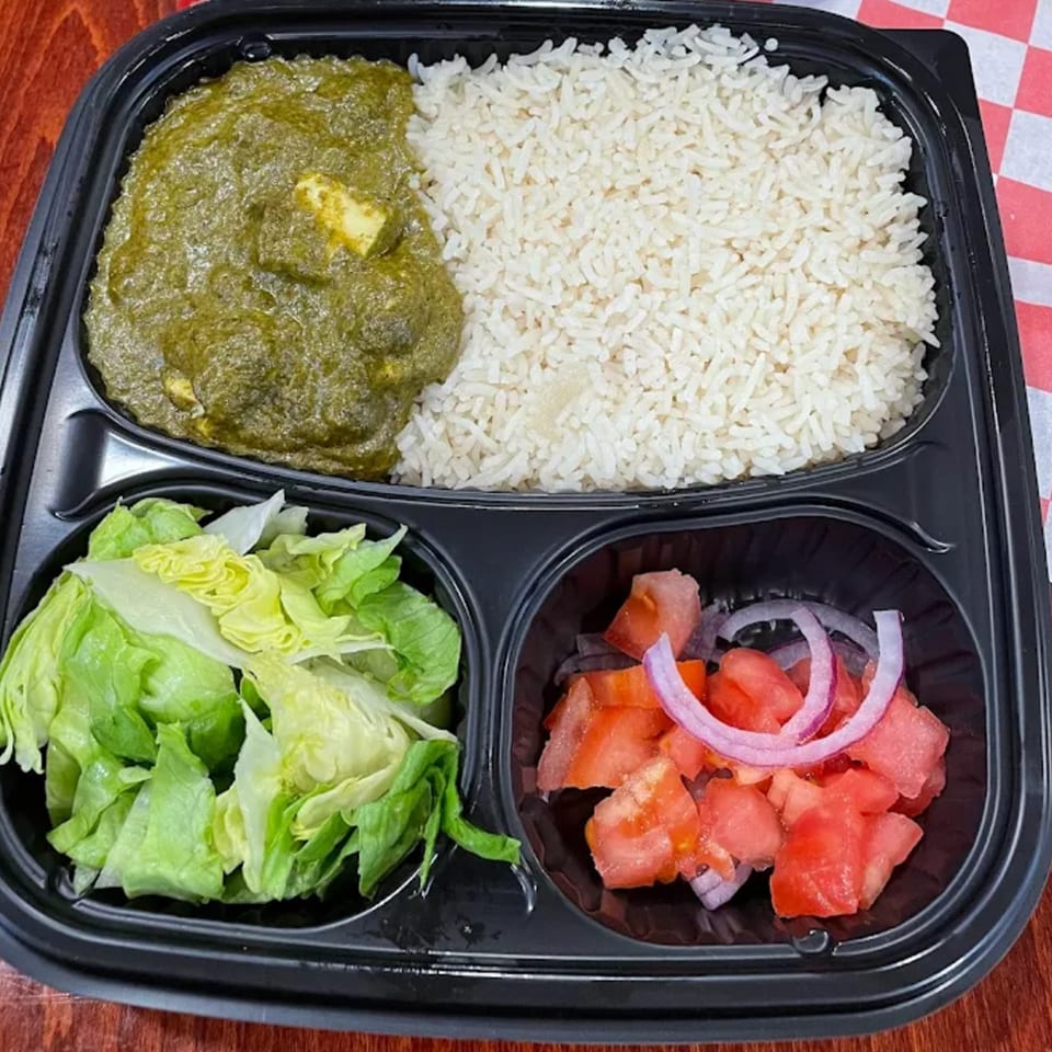 A takeout container with palak paneer, white rice, lettuce, and a tomato and onion salad.
