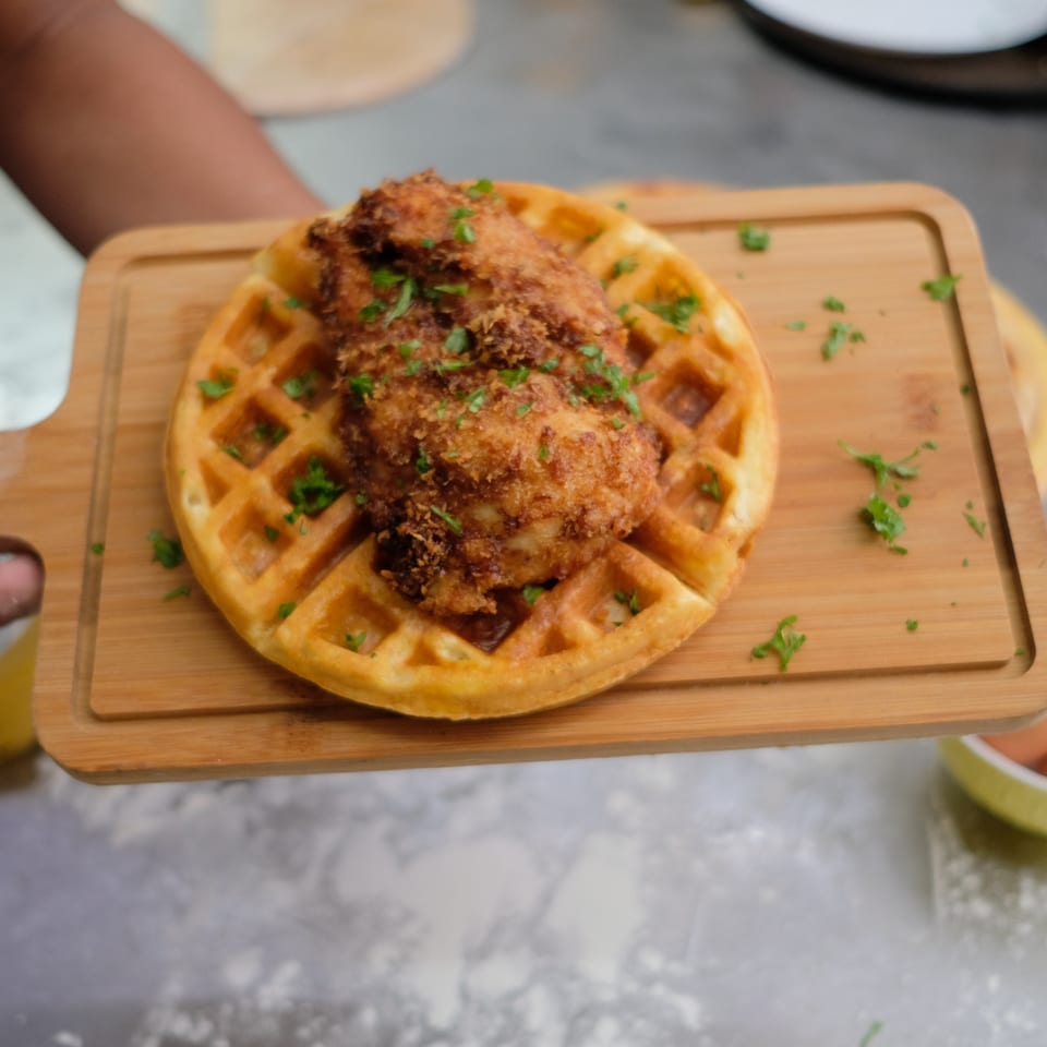Golden fried chicken and a waffle, garnished with parsley, on a wooden serving board.