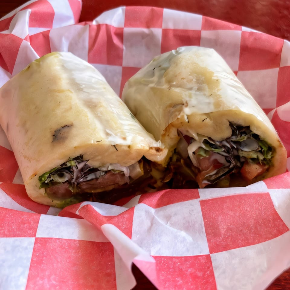 Two Ellenville Spice Fusion fried chicken wraps, cut in half, in a red and white checkered basket.