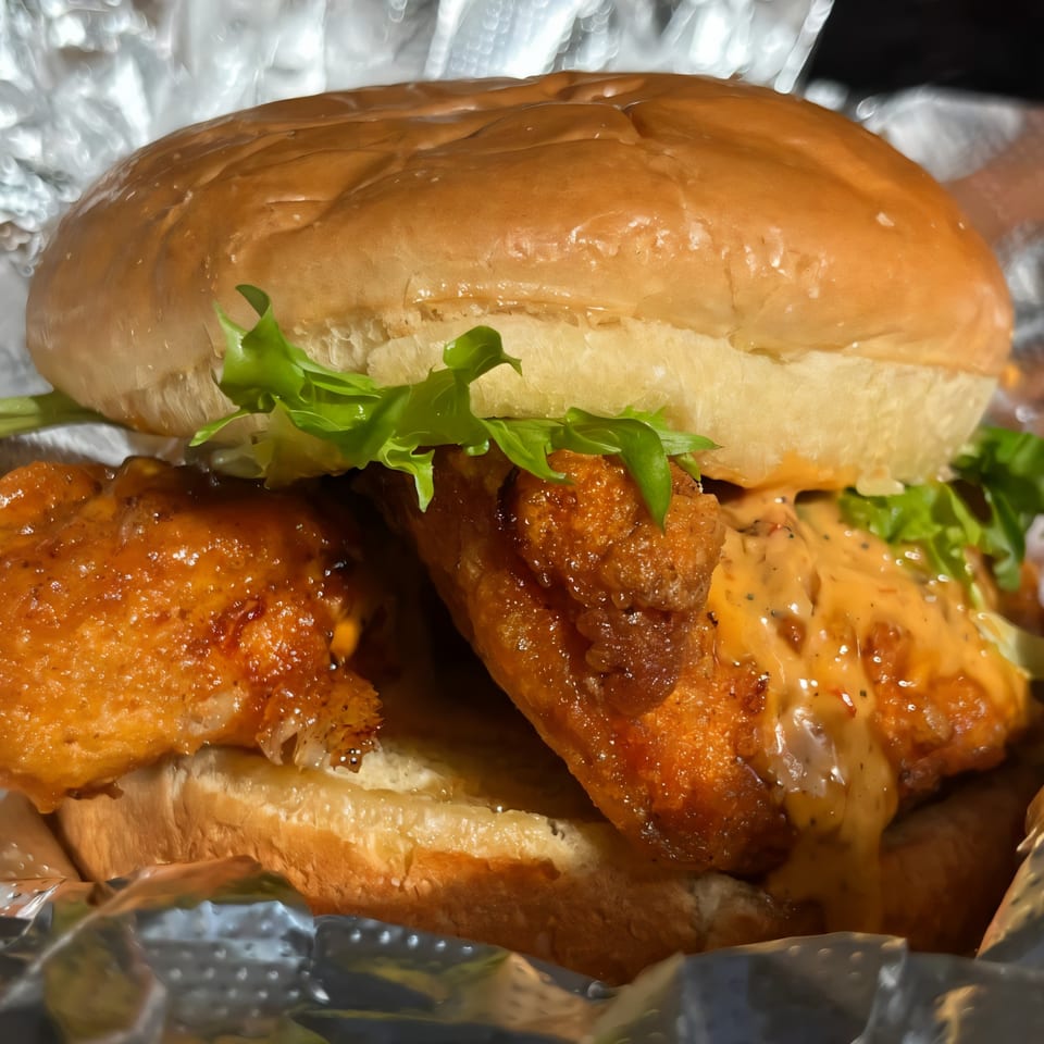 Ellenville Spice Fusion's fried chicken sandwich with lettuce and spicy sauce on a bun, wrapped in foil.
